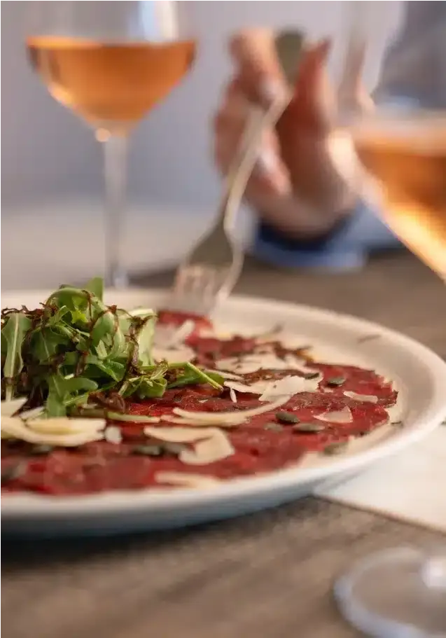 En tallerken carpaccio med ruccola og et glass rosévin på en restaurant på Las Colinas