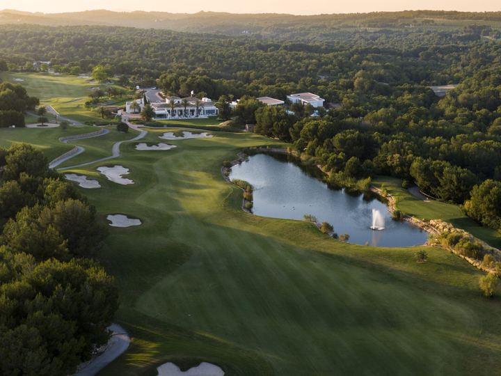 Luftfoto av klubbhuset på Las Colinas, innsjøen og fairwayene rundt, omgitt av furuskog